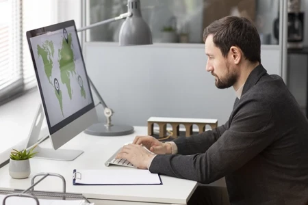 Connecting Cleantech Providers With Qualified Business Leads. Man analyzing global market opportunities on a computer screen in a modern workspace.