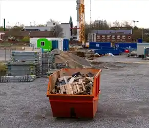 Reduce Construction Waste with Circular Solutions. Orange waste container filled with construction debris at a building site.