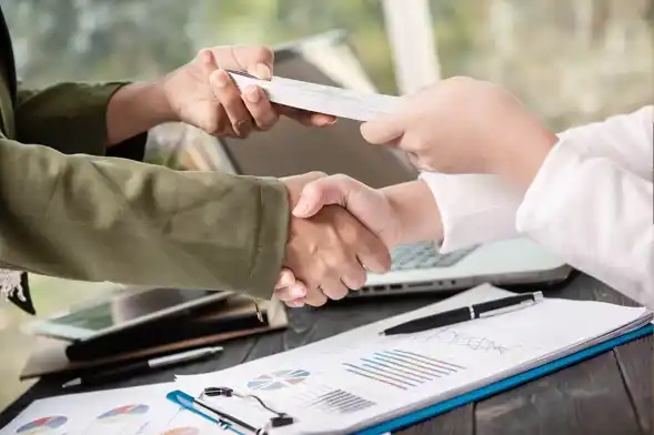 Join the Future of Sustainable Finance. Close-up of a handshake and contract exchange between professionals with financial documents on a desk.