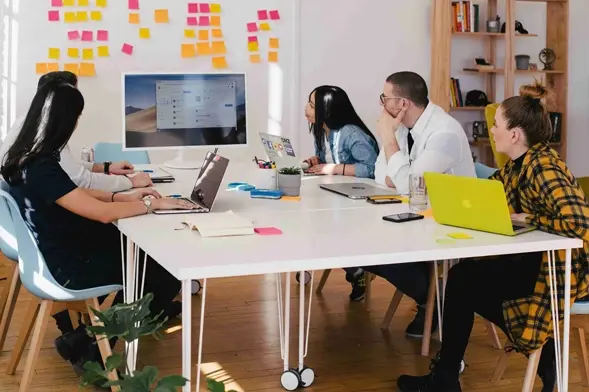 Collaborative Team Driving Sustainable Innovation. Diverse team collaborating around a table with laptops and sticky notes in a creative workspace.