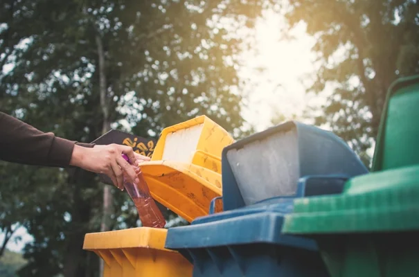 Smart Waste Management and Circular Materials. Person placing a plastic bottle into a yellow recycling bin outdoors.