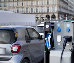 Electric Vehicle Charging Station Supporting Sustainable Building Mobility. Electric vehicle charging station with compact car in urban environment.
