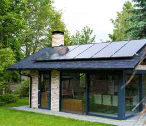 House with Solar Panels Demonstrating Energy Efficiency Solutions. Modern house with solar panels on the roof surrounded by trees.